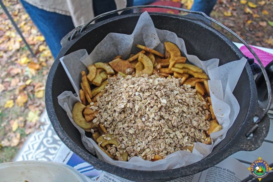 oatmeal mixture being added on top of apples in a Dutch oven