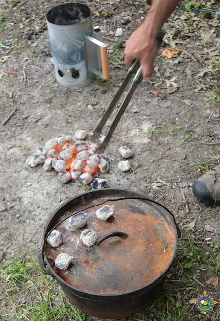 hot coals being place on the lid of a Dutch oven out at a campground