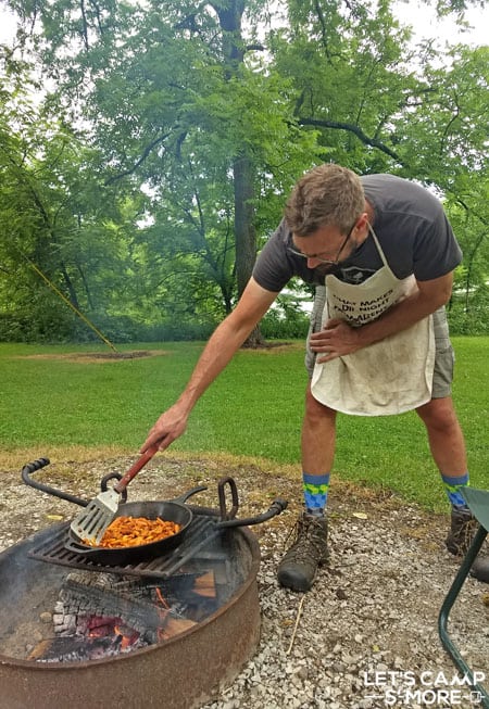 Man cooking in a cast iron pan over a campfire