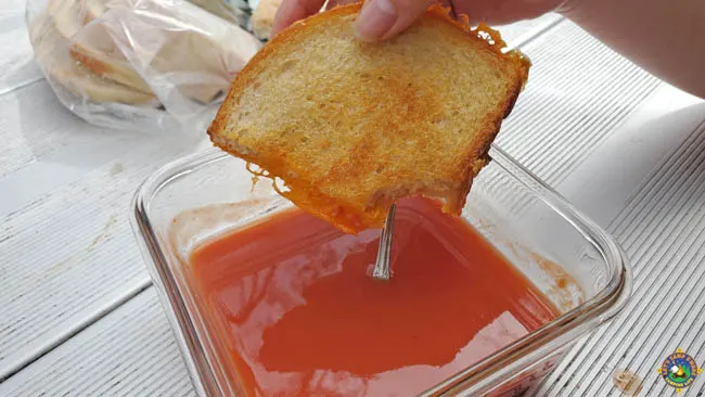cheese sandwich being dipped into a bowl of tomato soup