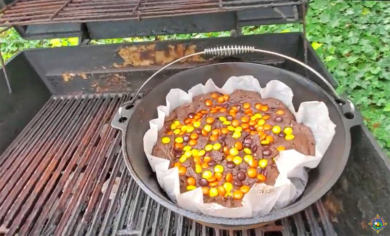 chocolate cake with candies on top being baked in a Dutch oven on a grill