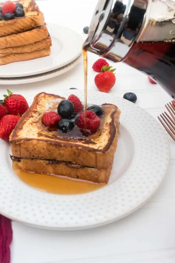 syrup being poured over a stack of french toast with berries on top